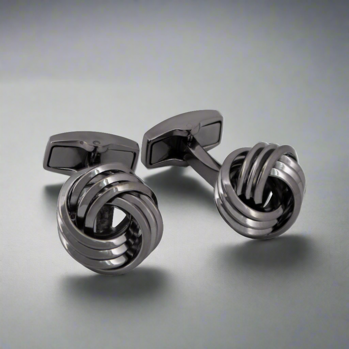 A pair of gunmetal-plated copper alloy cufflinks with a twisted knot design on a light background.